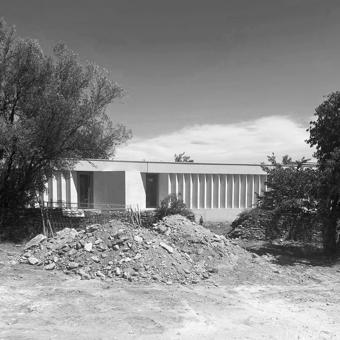 Chantier en noir et blanc : bâtiment bas à claire-voie derrière un tas de terre