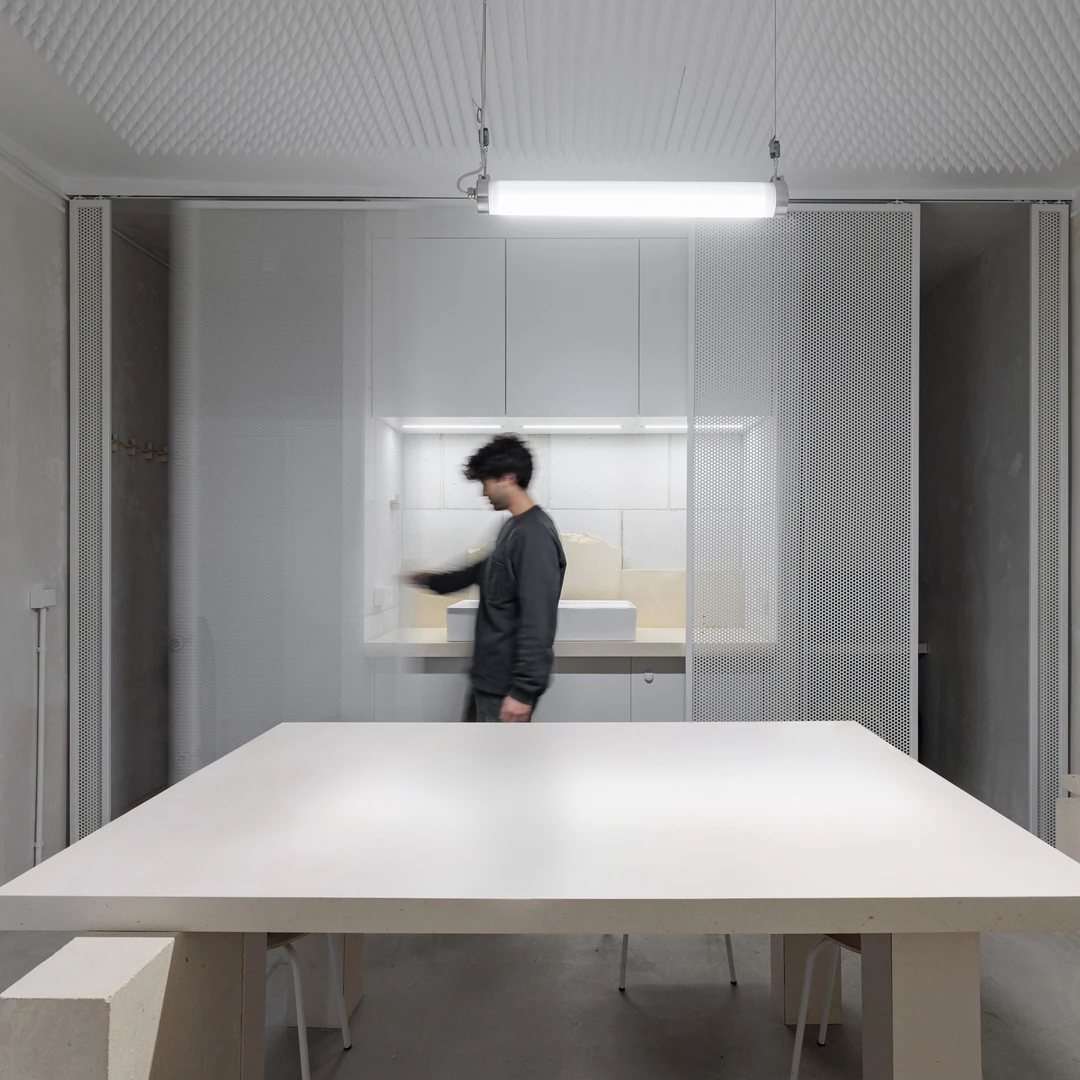 Intérieur blanc avec grande table en bois et un architecte devant un bureau éclairé
