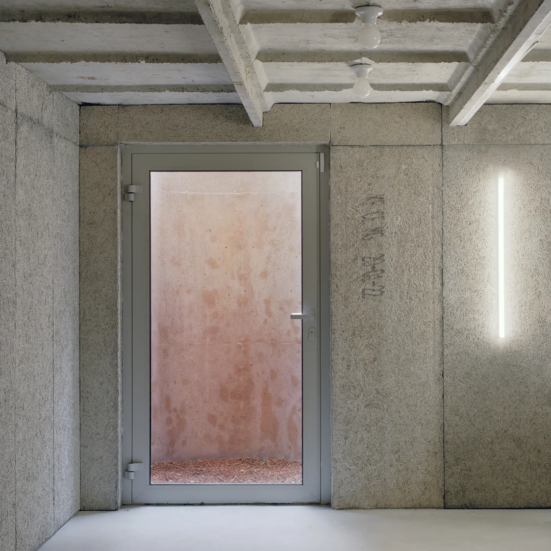 Pièce en béton brut, plafond à caissons et porte vitrée teintée de rose